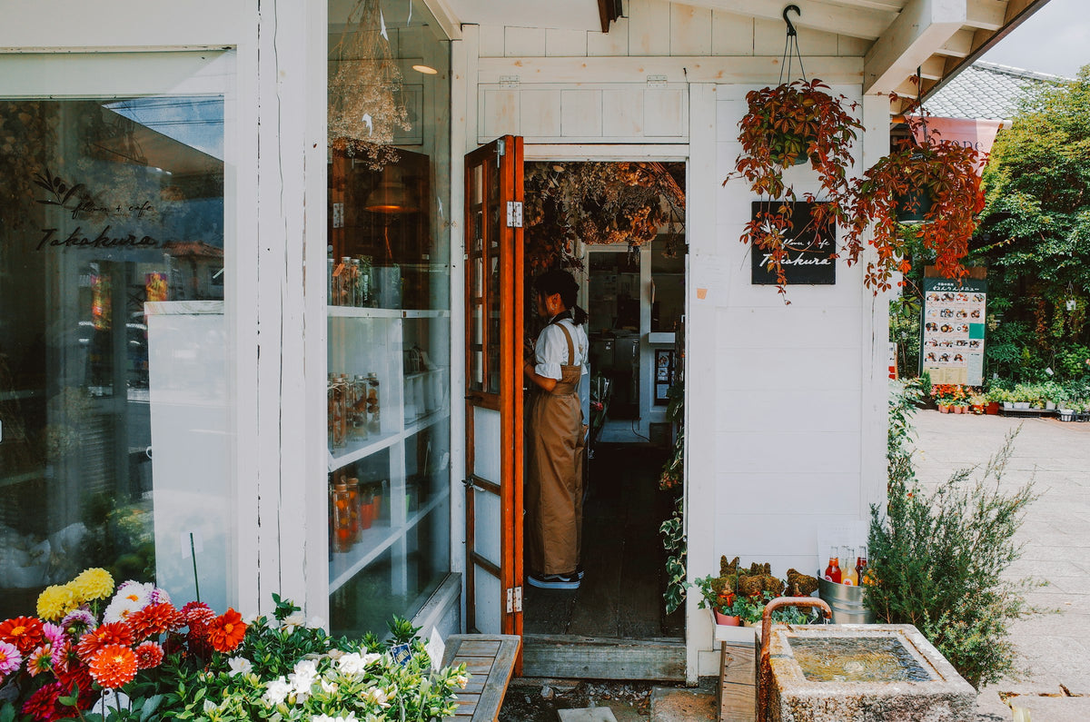 Woman standing in the doorway of a small flower shop surrounded by plants
