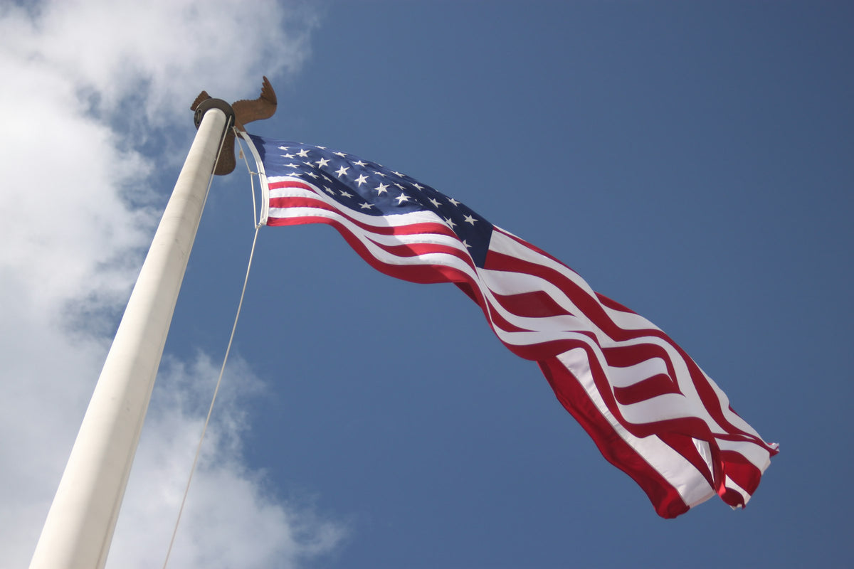 American flag flying from a white flagpole against a blue sky with clouds