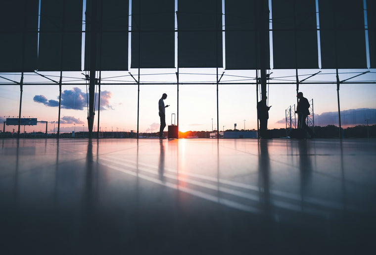 Silhouetted travelers with luggage in an airport terminal at sunset