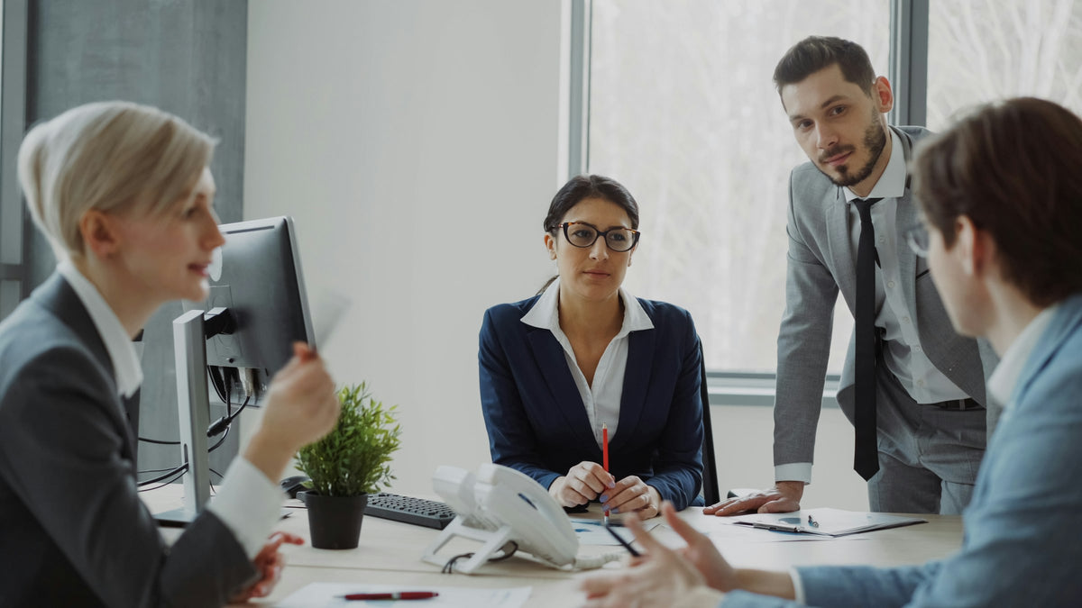 Four business professionals in suits meeting around a desk in a bright office