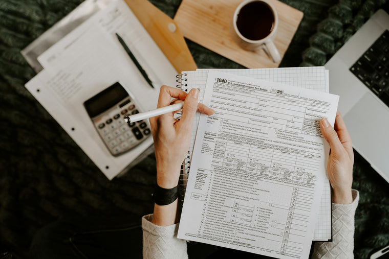Overhead view of a person reviewing tax forms with a calculator, coffee and laptop