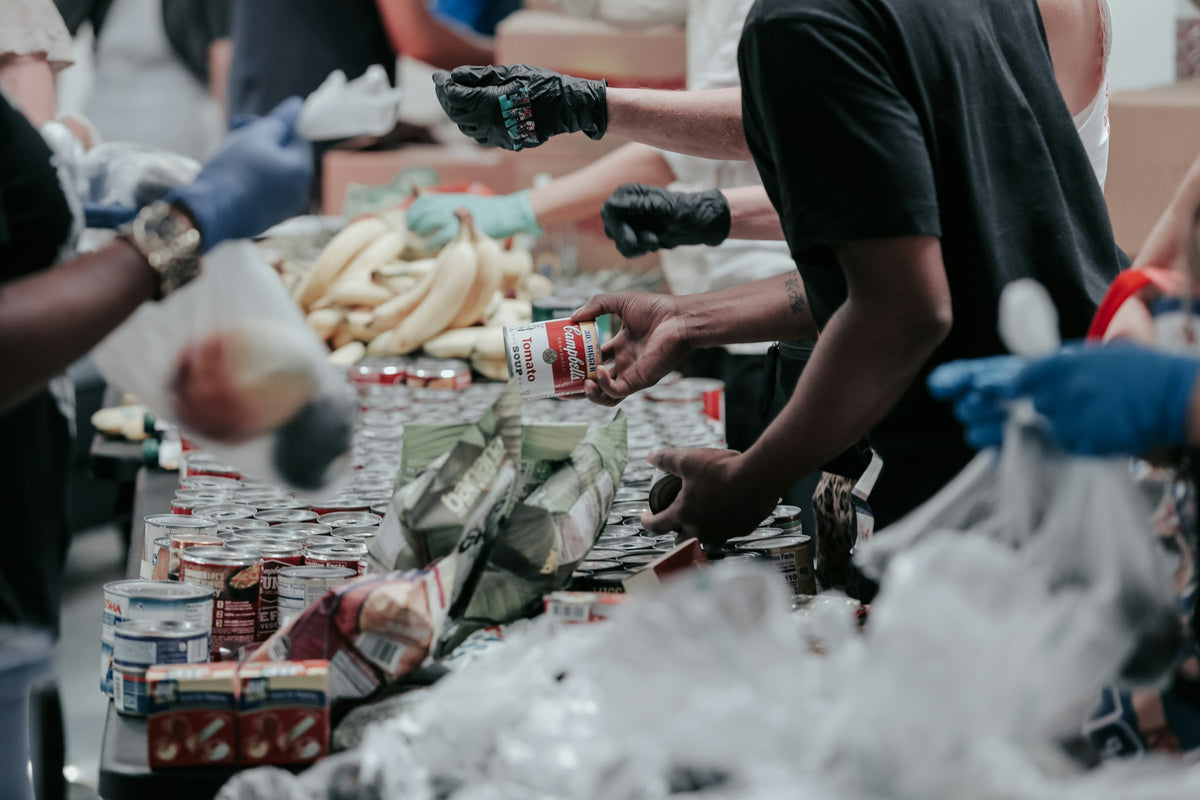 Volunteers in gloves sorting canned food and produce at a donation table