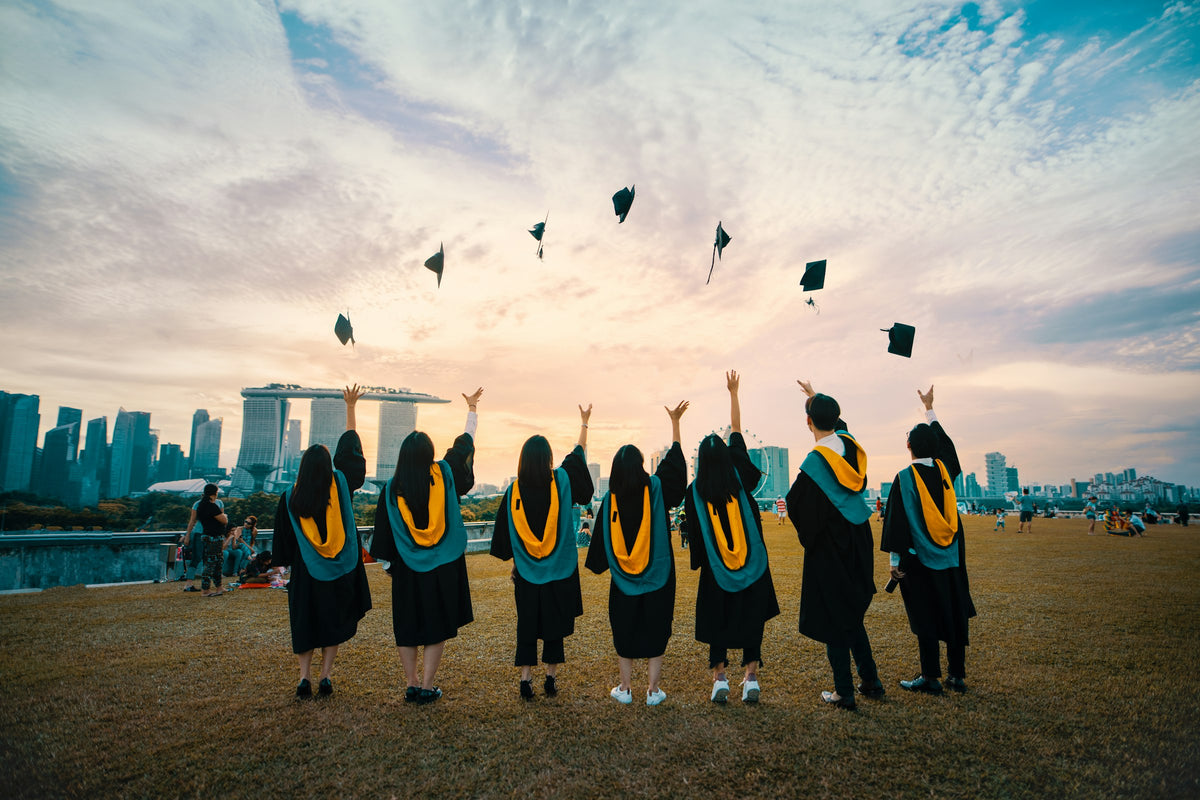 Graduates in gowns throwing their caps into the air against a sunset sky