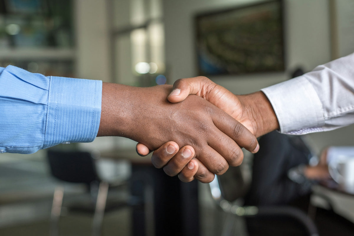 Close-up of two people in dress shirts shaking hands in an office