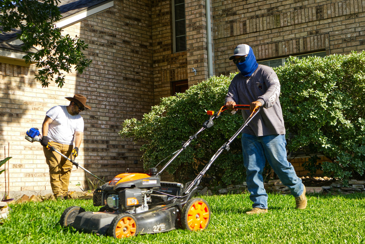 Two landscaping workers mowing and trimming the lawn outside a brick building