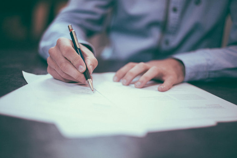 Close-up of a hand writing on paper documents with a pen at a desk