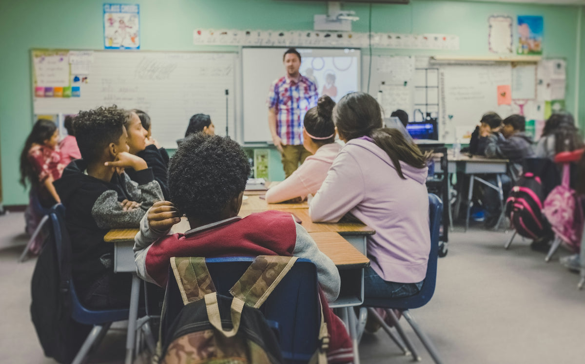 Diverse group of children at desks listening to a teacher in a classroom