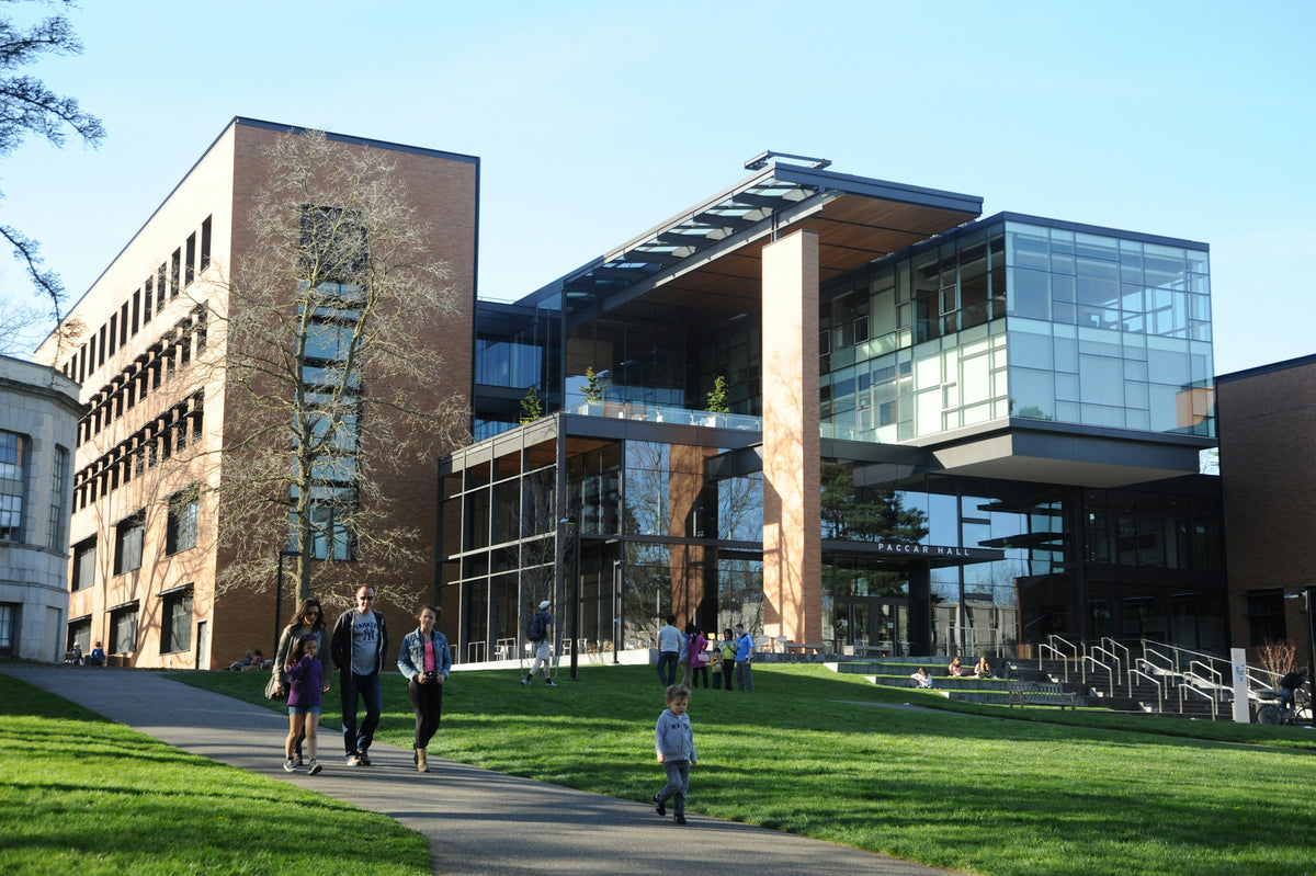 Students walking along a path past modern university buildings on a sunny day